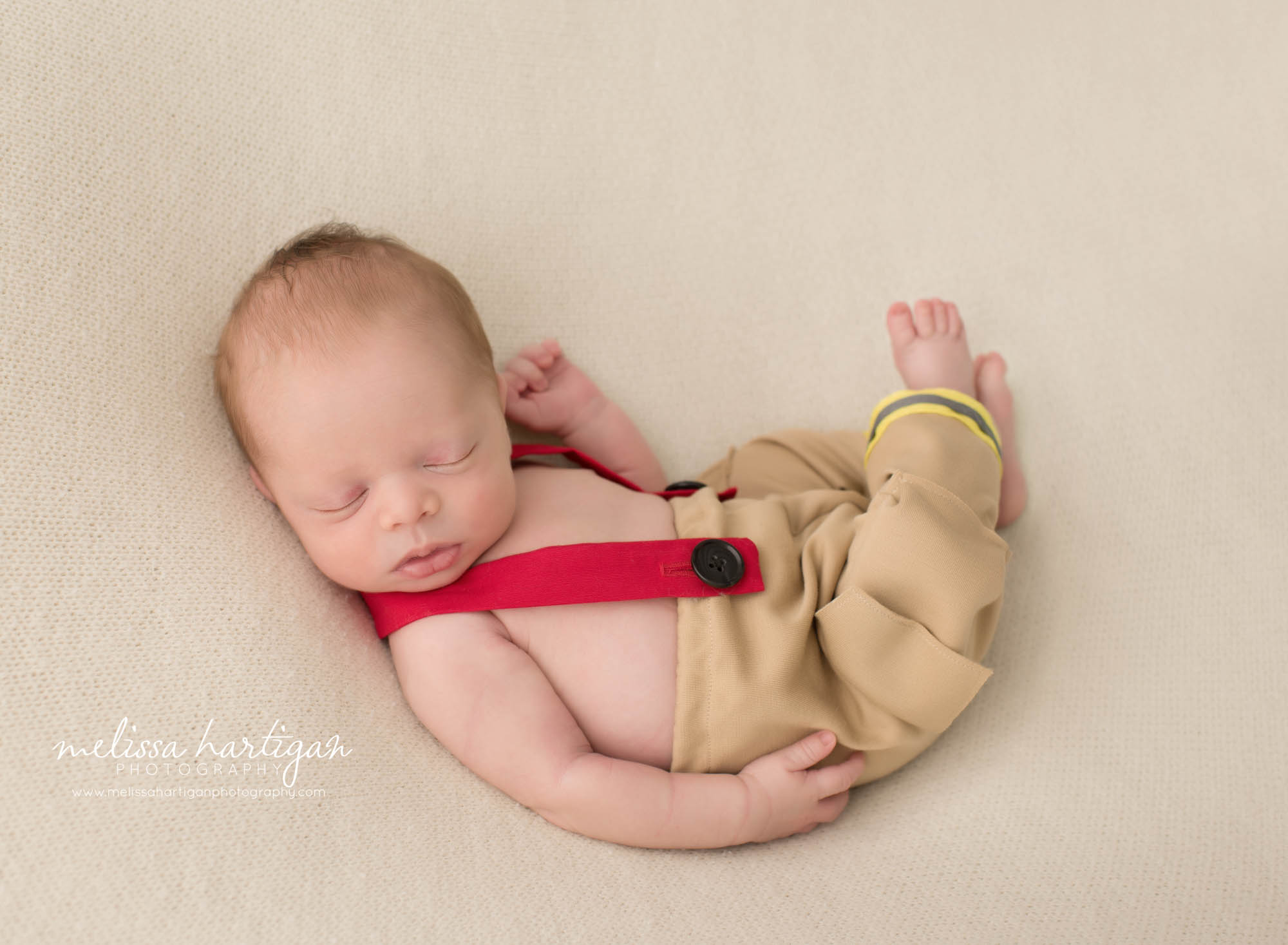 Newborn baby boy posed on backdrop wearing fire fighter outfit