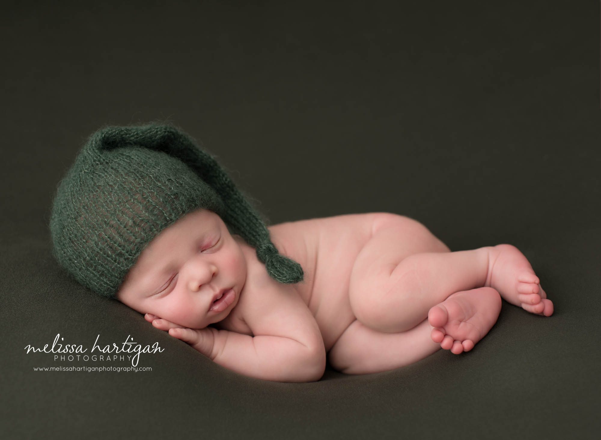 Newborn baby boy posed on green backdrop wearing green sleepy cap