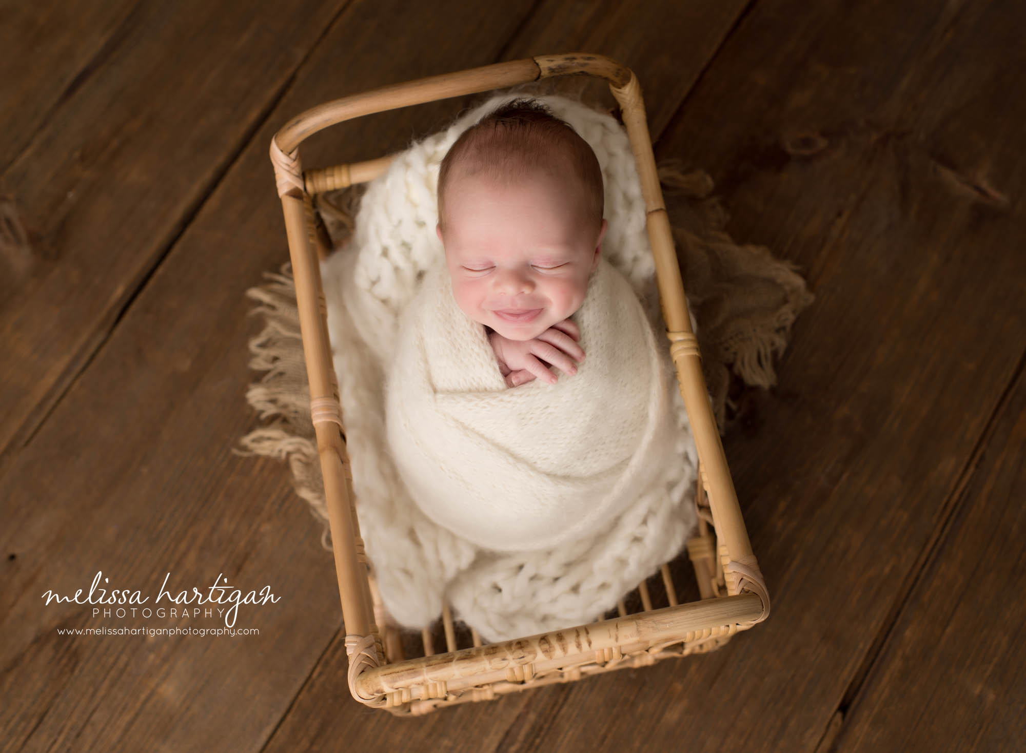 Newborn baby boy smiling posed in basket wrapped in cream wrap