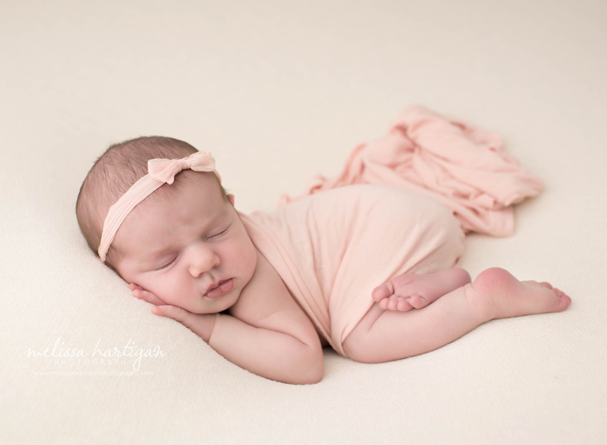 Newborn baby girl posed on tummy with pink layer draped over her